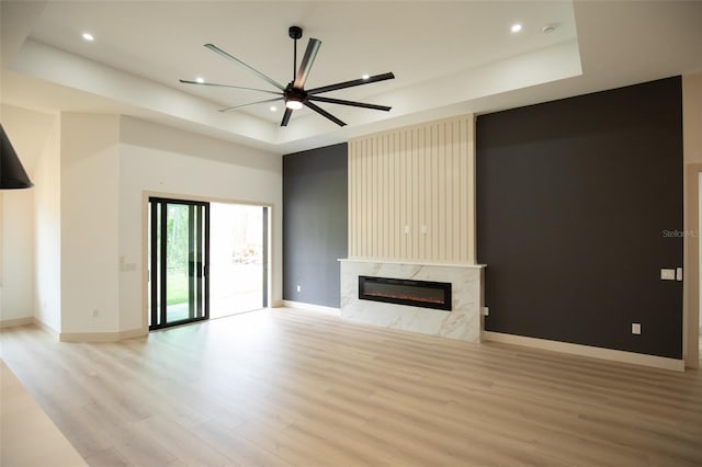 unfurnished living room with baseboards, a high end fireplace, a tray ceiling, light wood-type flooring, and recessed lighting