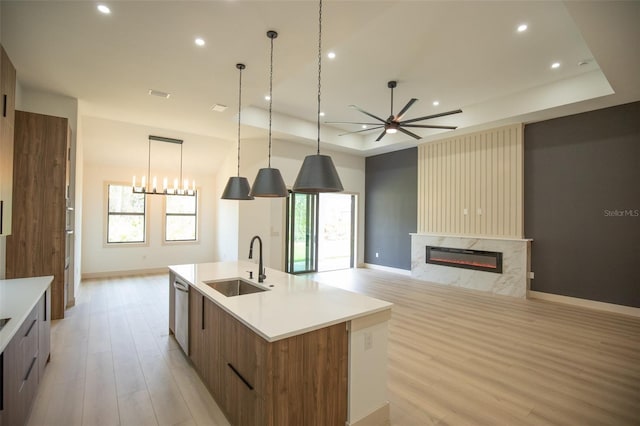 kitchen with a raised ceiling, light wood-style flooring, modern cabinets, a sink, and a high end fireplace