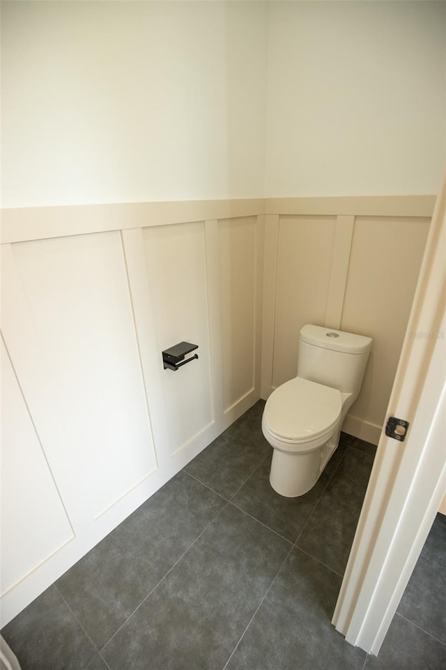 bathroom with wainscoting, a decorative wall, toilet, and tile patterned floors