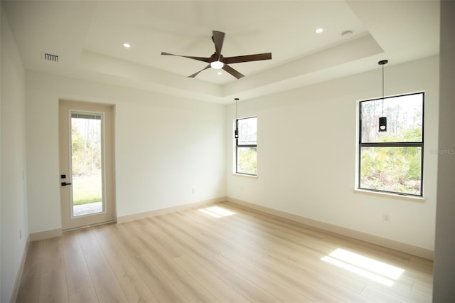 unfurnished room featuring light wood-type flooring, visible vents, a tray ceiling, and baseboards