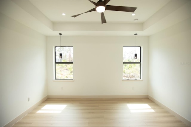 empty room with light wood finished floors, baseboards, a raised ceiling, and recessed lighting