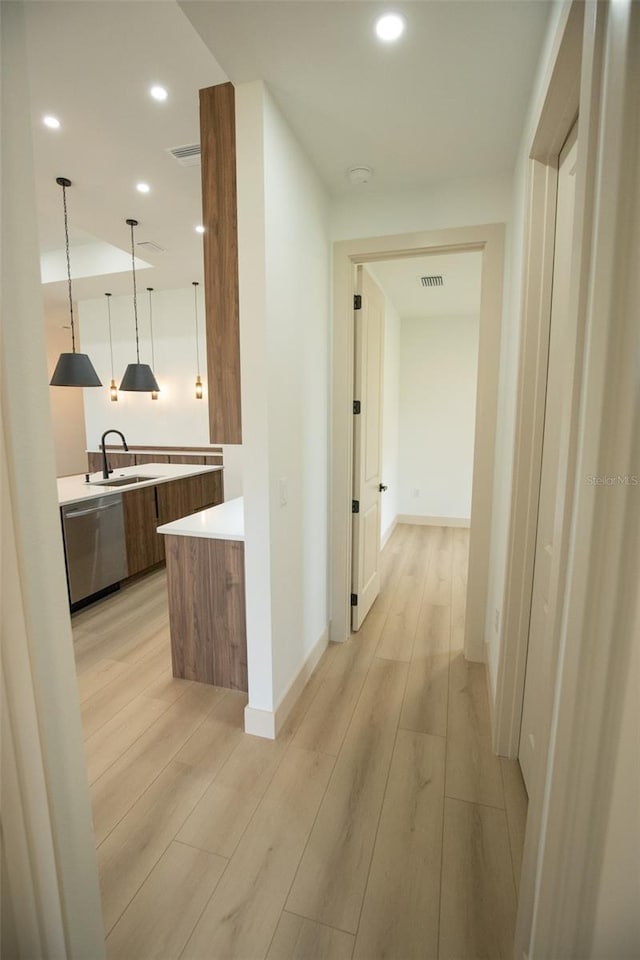 hall with light wood-style flooring, a sink, and recessed lighting