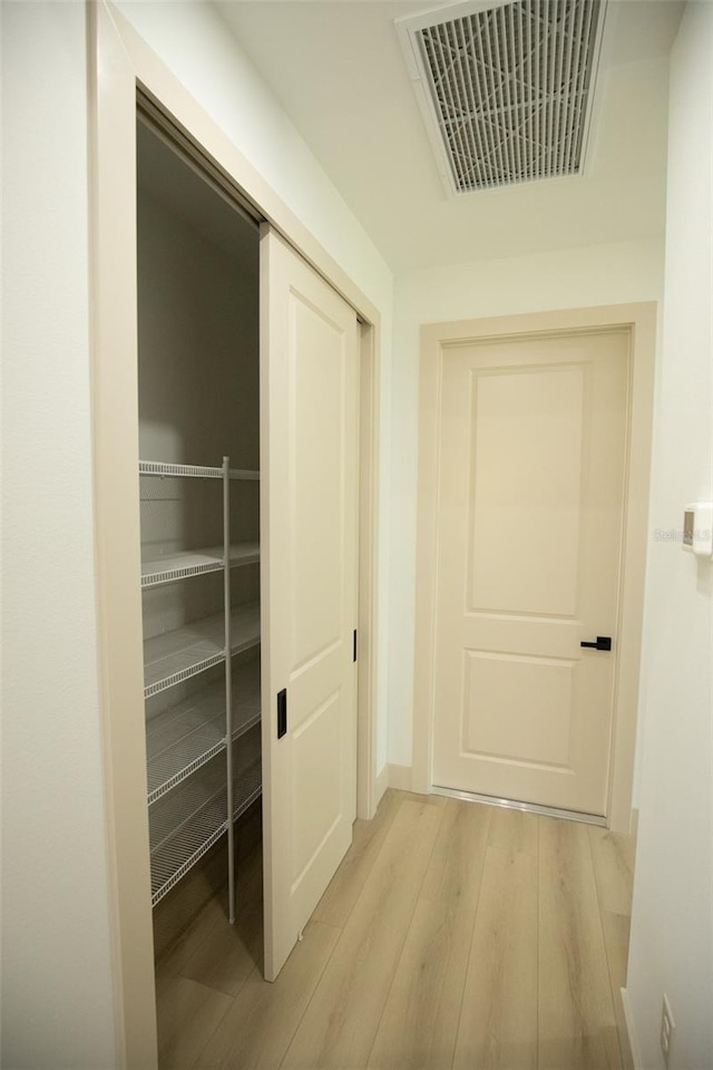 hall featuring light wood-type flooring, visible vents, and baseboards