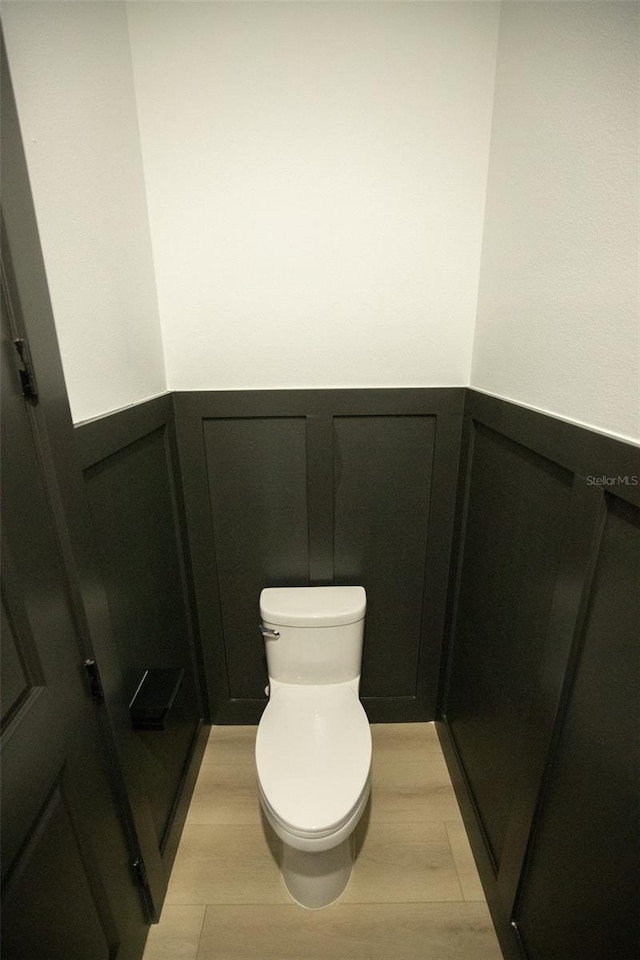 bathroom featuring toilet, a decorative wall, and wainscoting