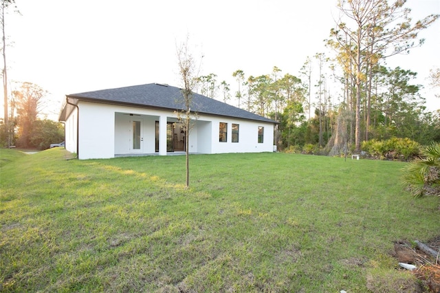 rear view of property featuring a ceiling fan, a yard, and stucco siding