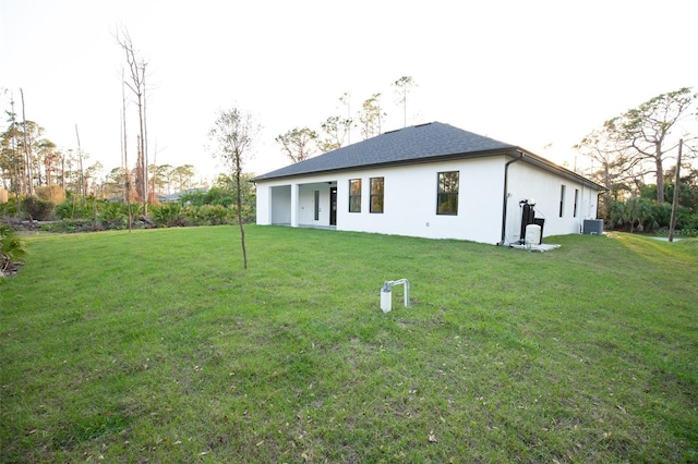 rear view of property with central AC, a yard, and stucco siding