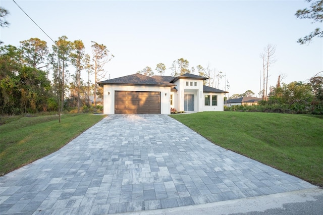 prairie-style house with a garage, decorative driveway, a front yard, and stucco siding