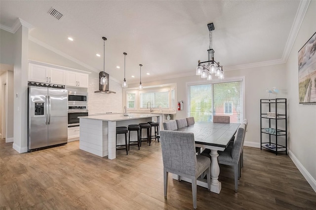 dining space with vaulted ceiling, ornamental molding, wood finished floors, and visible vents