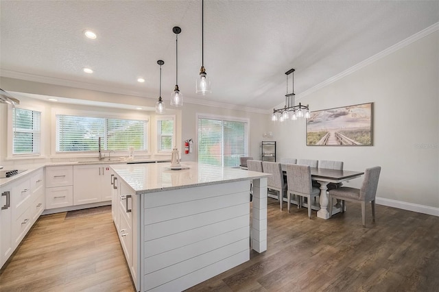 kitchen featuring crown molding, a kitchen island, a sink, light stone countertops, and light wood-type flooring