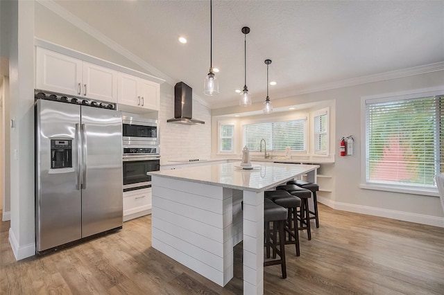 kitchen featuring appliances with stainless steel finishes, a center island, ornamental molding, and wall chimney exhaust hood