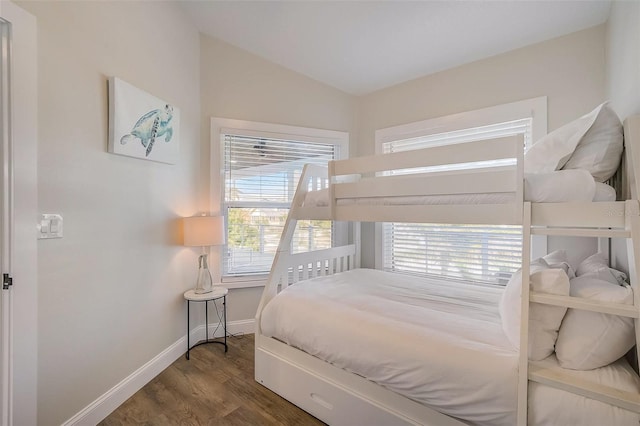 bedroom featuring lofted ceiling, multiple windows, wood finished floors, and baseboards