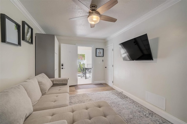 living room featuring a textured ceiling, visible vents, wood finished floors, and ornamental molding