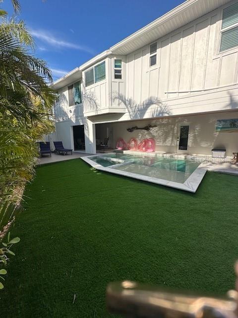 rear view of property featuring a yard, board and batten siding, a patio area, and an outdoor pool