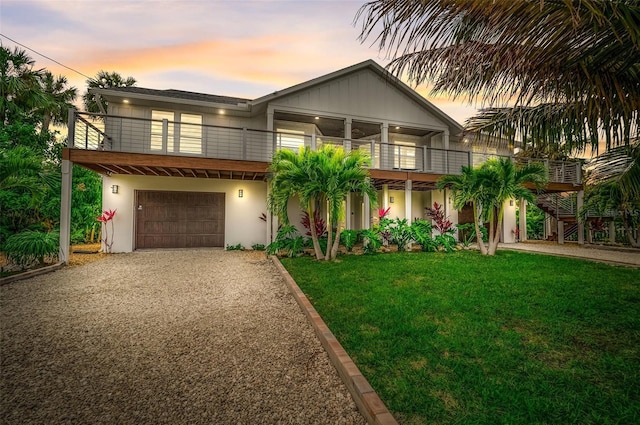 view of front of home featuring a front yard, gravel driveway, a balcony, and stucco siding