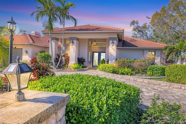 mediterranean / spanish home with a garage, a tiled roof, french doors, and stucco siding