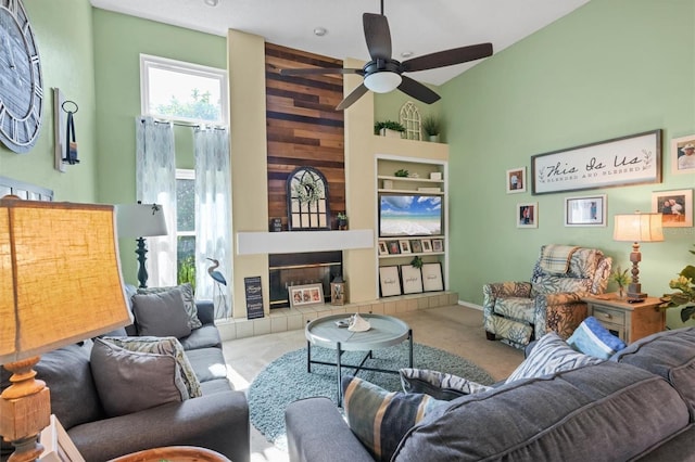 living area with built in shelves, carpet, a fireplace, a high ceiling, and ceiling fan