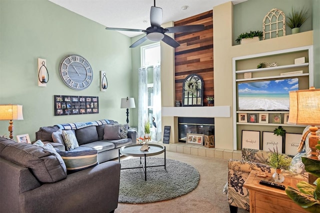 carpeted living room with ceiling fan, a fireplace, a towering ceiling, and built in features