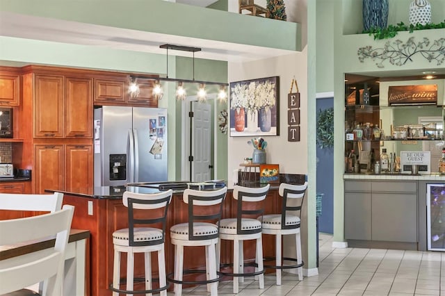 bar featuring wet bar, light tile patterned flooring, decorative light fixtures, and stainless steel fridge with ice dispenser