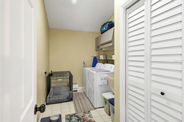 laundry area with cabinet space, light tile patterned floors, baseboards, washing machine and clothes dryer, and a textured ceiling