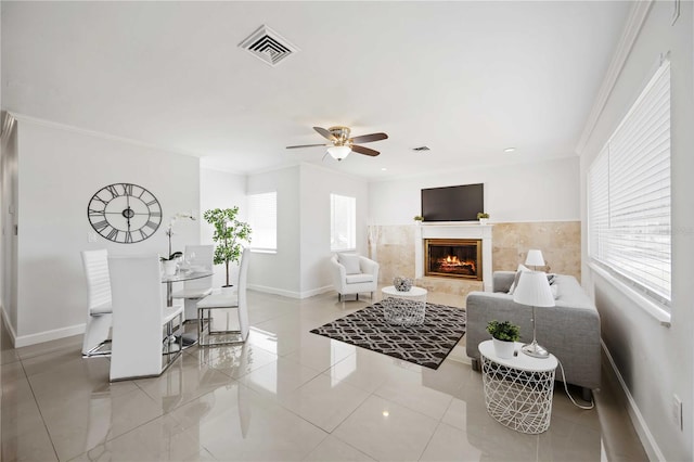 living room featuring a tile fireplace, visible vents, crown molding, and baseboards