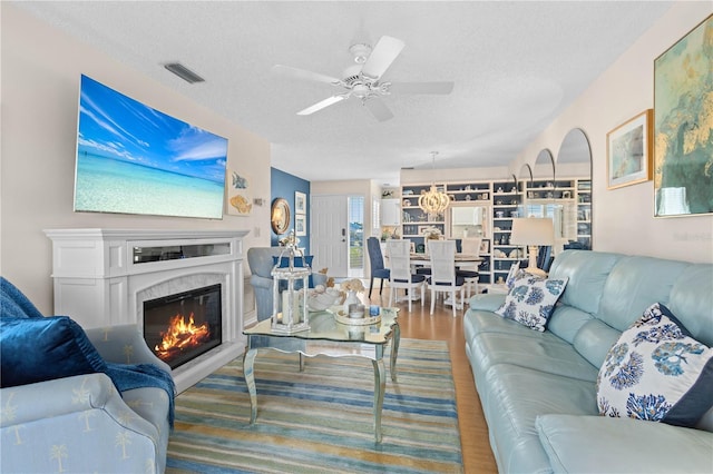 living room featuring a fireplace, visible vents, ceiling fan, a textured ceiling, and wood finished floors