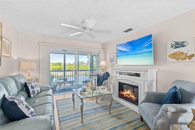 living area with a ceiling fan, visible vents, a textured ceiling, and a glass covered fireplace