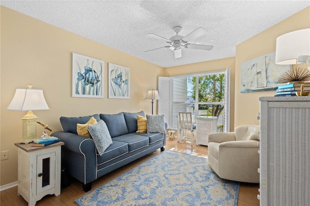 living area featuring a ceiling fan, a textured ceiling, baseboards, and wood finished floors