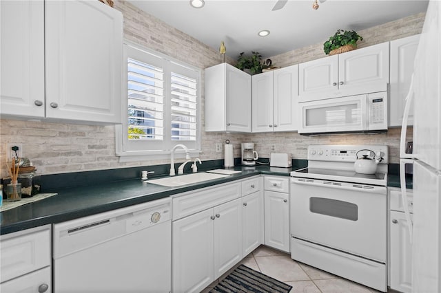 kitchen featuring white appliances, light tile patterned floors, white cabinets, dark countertops, and a sink