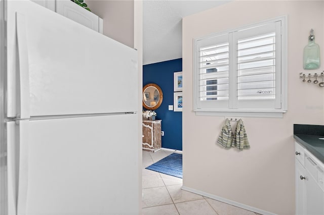 kitchen featuring baseboards, light tile patterned flooring, white cabinets, and freestanding refrigerator