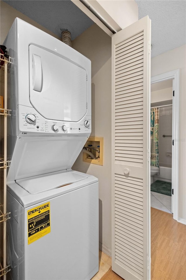 laundry area with stacked washer and clothes dryer, baseboards, light wood finished floors, and laundry area