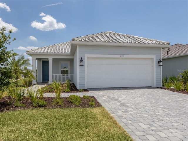 view of front of property featuring an attached garage, covered porch, decorative driveway, and a tiled roof