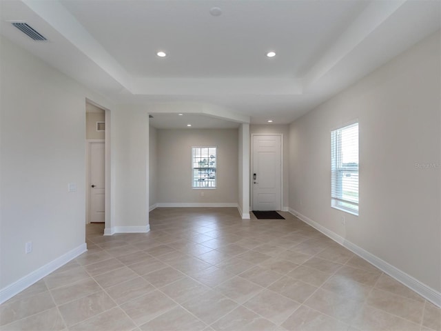 empty room with a tray ceiling, recessed lighting, visible vents, and baseboards