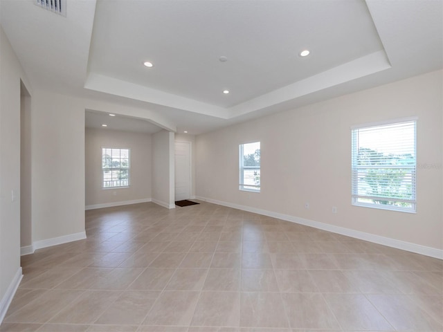 empty room with a tray ceiling, visible vents, and baseboards