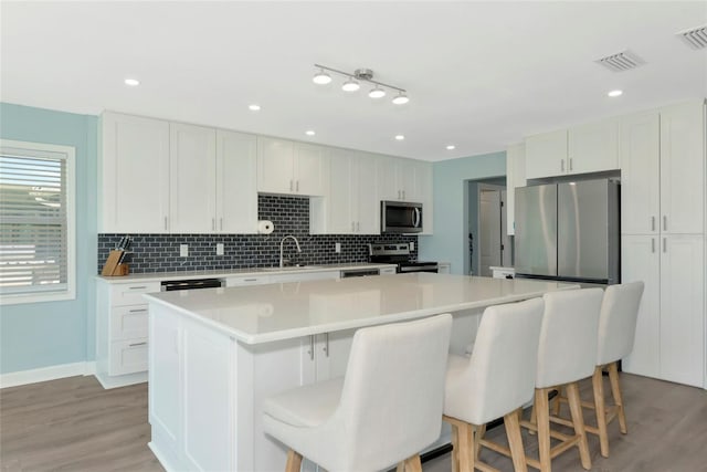 kitchen featuring a kitchen island, a kitchen breakfast bar, a sink, stainless steel appliances, and backsplash