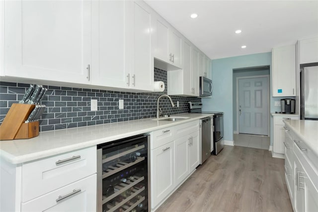 kitchen with appliances with stainless steel finishes, wine cooler, light countertops, and a sink