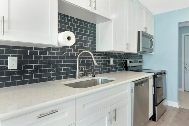 kitchen with light stone counters, decorative backsplash, appliances with stainless steel finishes, white cabinetry, and a sink