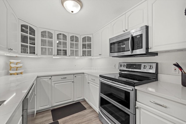 kitchen featuring appliances with stainless steel finishes, light wood-type flooring, white cabinetry, and glass insert cabinets