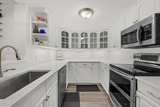 kitchen with light wood-style flooring, stainless steel appliances, a sink, white cabinets, and glass insert cabinets