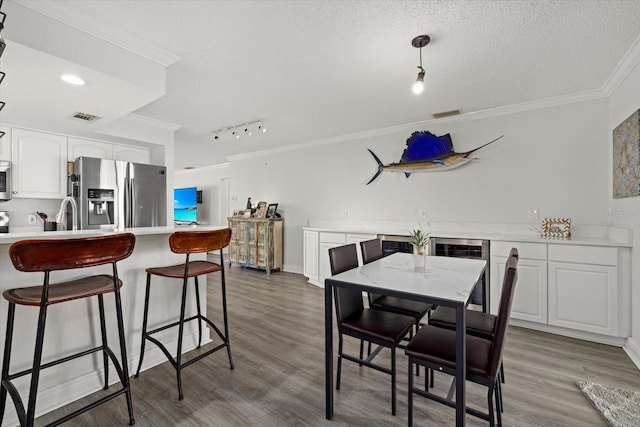 dining space featuring ornamental molding, beverage cooler, a textured ceiling, and wood finished floors