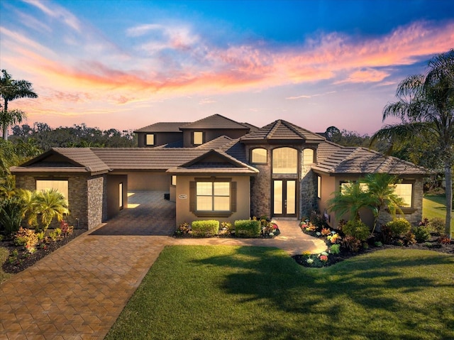 prairie-style house with stone siding, french doors, decorative driveway, and a lawn