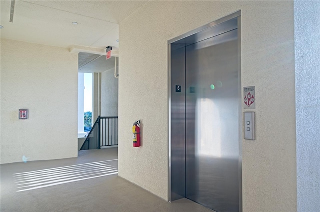 corridor featuring a textured wall, an upstairs landing, and elevator