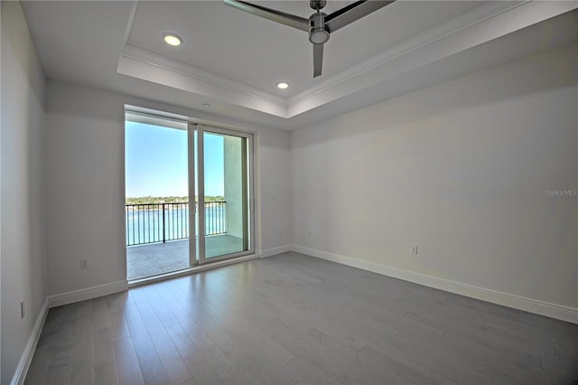 empty room featuring recessed lighting, dark wood-style flooring, baseboards, a tray ceiling, and crown molding