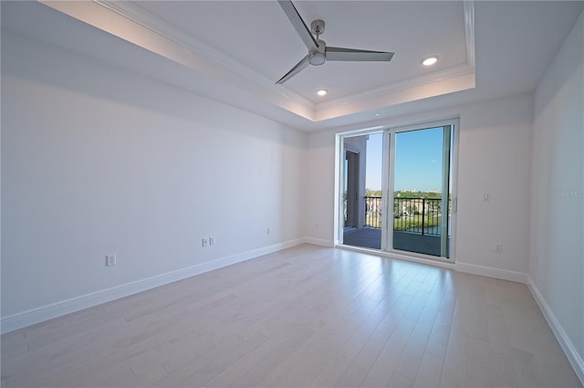 spare room with baseboards, a tray ceiling, light wood-style floors, and crown molding