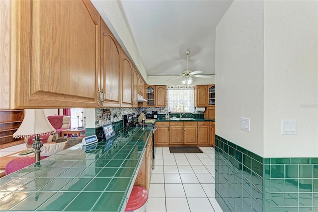 kitchen featuring electric range, tile counters, ceiling fan, a sink, and light tile patterned flooring