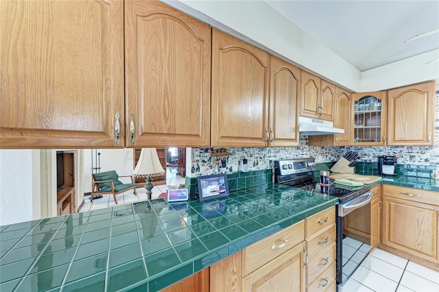 kitchen featuring light tile patterned floors, glass insert cabinets, stainless steel electric stove, under cabinet range hood, and backsplash