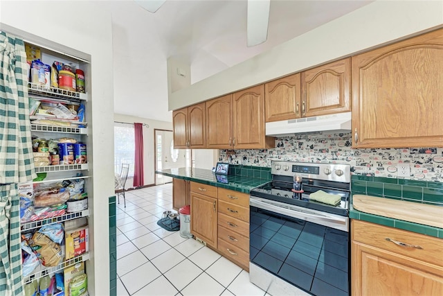 kitchen featuring tile countertops, decorative backsplash, light tile patterned flooring, stainless steel range with electric cooktop, and under cabinet range hood