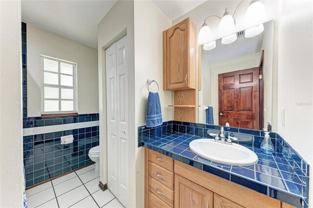 bathroom with tile patterned flooring, toilet, vanity, tile walls, and a closet