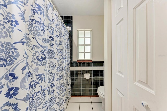 bathroom featuring toilet, a shower with shower curtain, tile patterned flooring, and tile walls