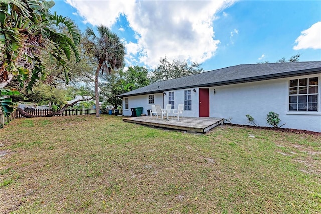 rear view of house with a shingled roof, fence, a deck, a yard, and stucco siding