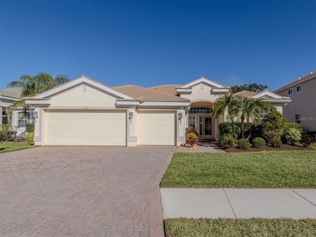 view of front of house with decorative driveway, stucco siding, an attached garage, a front yard, and a tiled roof